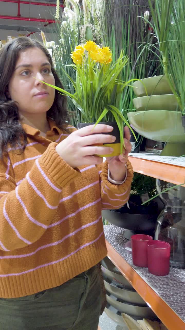 Young woman buying a small decorative artificial plant in a store.