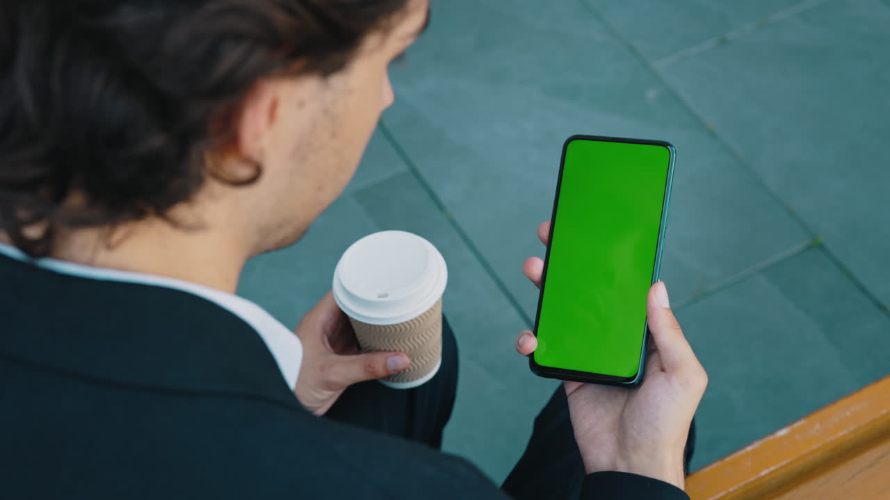 Man Holding Smartphone with Green Screen and Coffee Cup Outdoors