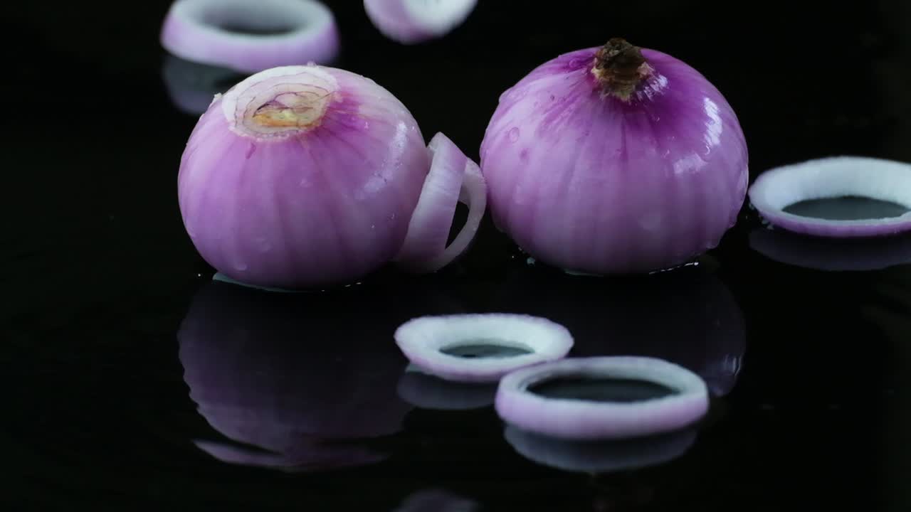 Onion Rings Falling onto Two Onions on a Black Water Covered Surface