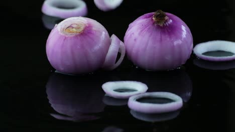 onion rings falling onto two onions on a black water covered surface