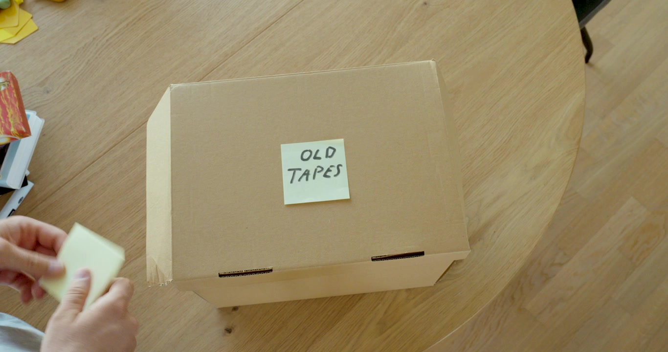 Person lægger gamle VHS-bånd i en papkasse til opbevaring. Ideel til nostalgi, gamle minder, arkivering, oprydning og retro-teknologi