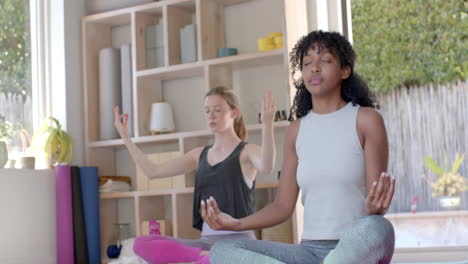 focused diverse fitness women exercising and meditating on mat in white room, slow motion