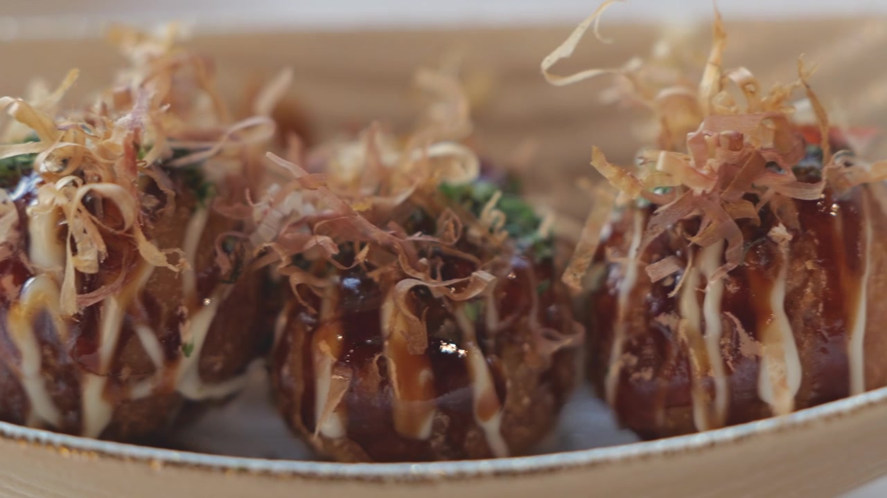 Primo piano di takoyaki appena cucinati, conditi con salsa saporita, maionese e scaglie delicate, serviti caldi con una consistenza appetitosa e dorata.