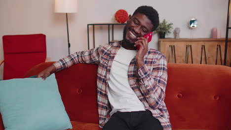 Young-adult-african-american-man-enjoying-talking-mobile-phone-conversation-with-friends-at-home