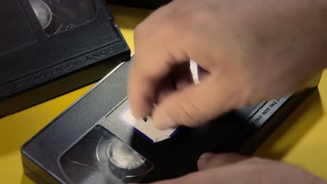 aplicando una etiqueta blanca en una cinta vhs, con el texto escrito a mano 2000s