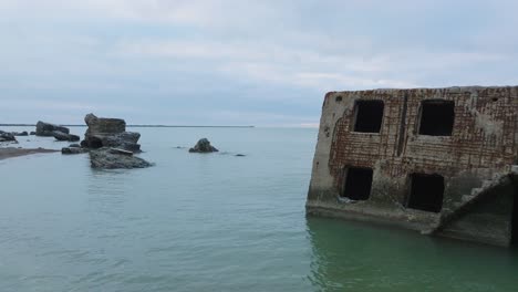 aerial view of abandoned seaside fortification buildings at karosta northern forts on the beach of baltic sea , waves splash, overcast day, wide drone shot moving forward low