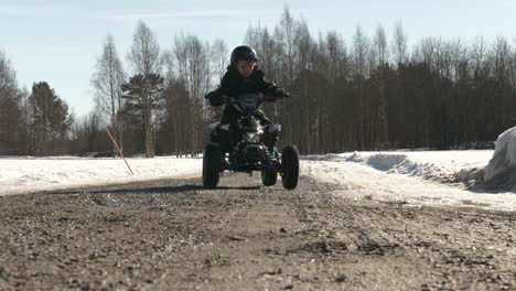 young caucasian boy riding mini atv on dirt road in snow