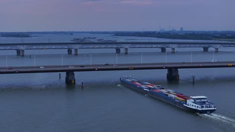 Moerdijk-Brücken-Mit-Autos,-Unter-Denen-Ein-Frachtschiff-Mit-Frachtcontainern-Den-Fluss-Entlang-Fährt