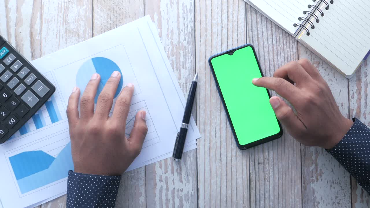 Vista superior de la mano del hombre con un teléfono inteligente en el escritorio de la oficina