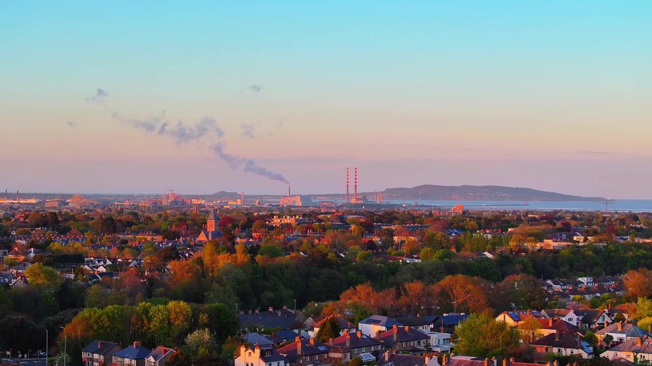 Suburban Dublin under evening light, with smokestacks visible on the horizon. Suitable for urban development and environmental documentaries.