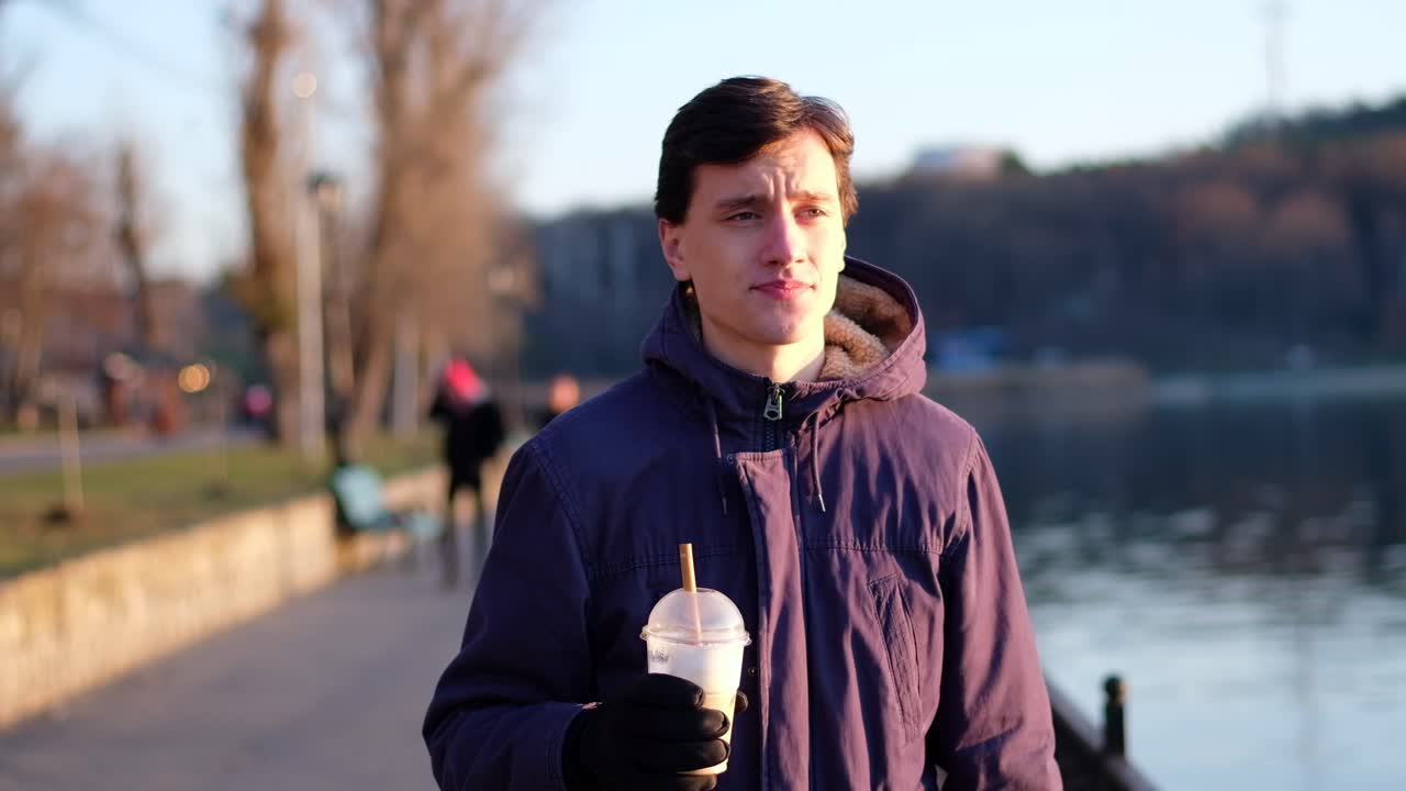 Young man walking in the park and drink ice coffee from a cup using bamboo straw