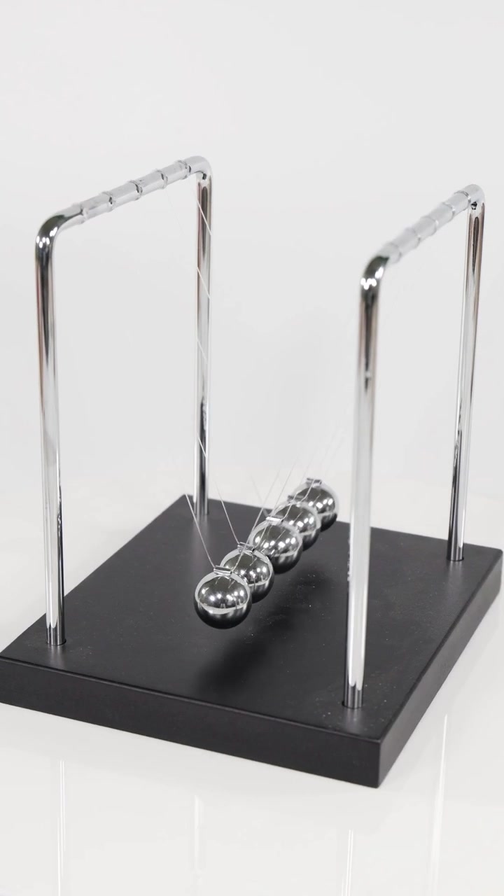 A vertical close-up showing chrome spheres swinging and colliding on a black base.