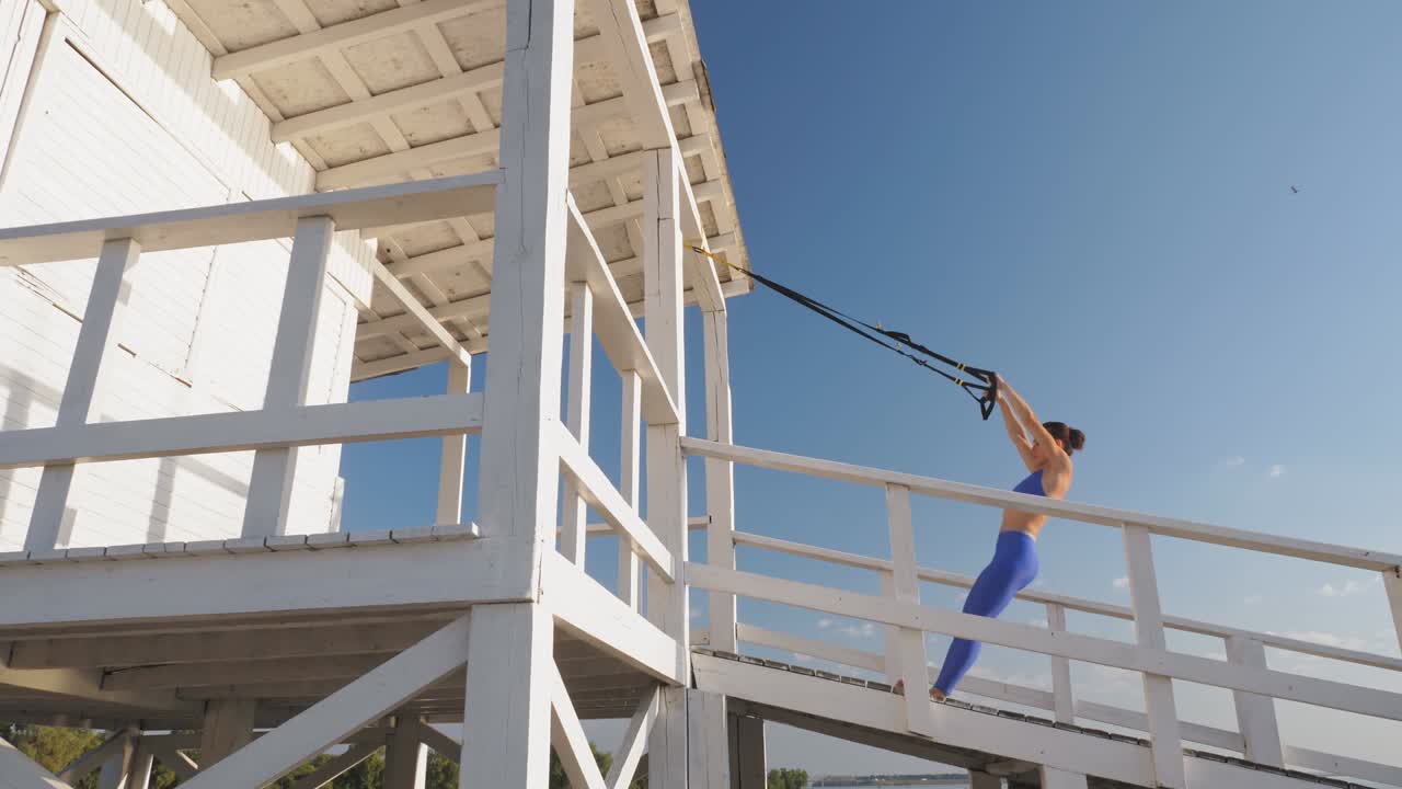 entrenamiento al aire libre. correas de suspensión. entrenamiento con correas. mujer joven atlética está haciendo ejercicios de resistencia de todo el cuerpo usando cuerdas en bucle trx, en la playa durante la puesta o el amanecer. entrenamiento de fitness al aire abierto. concepto de estilo de vida saludable. deporte matutino