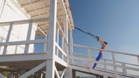 workout outdoors. suspension straps. workout with straps. athletic young woman is doing all-body resistance exercises using looped ropes trx, at the beach during sunset or sunrise. fitness training outdoors. healthy lifestyle concept. morning sport