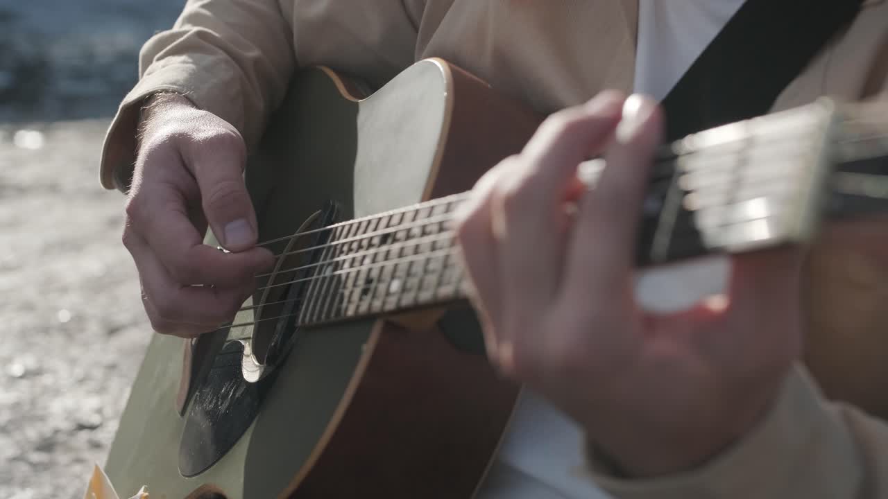 joven tocando la guitarra sentado en la orilla de un río de montaña sobre un fondo de rocas. concepto de libertad lugar de relajación.