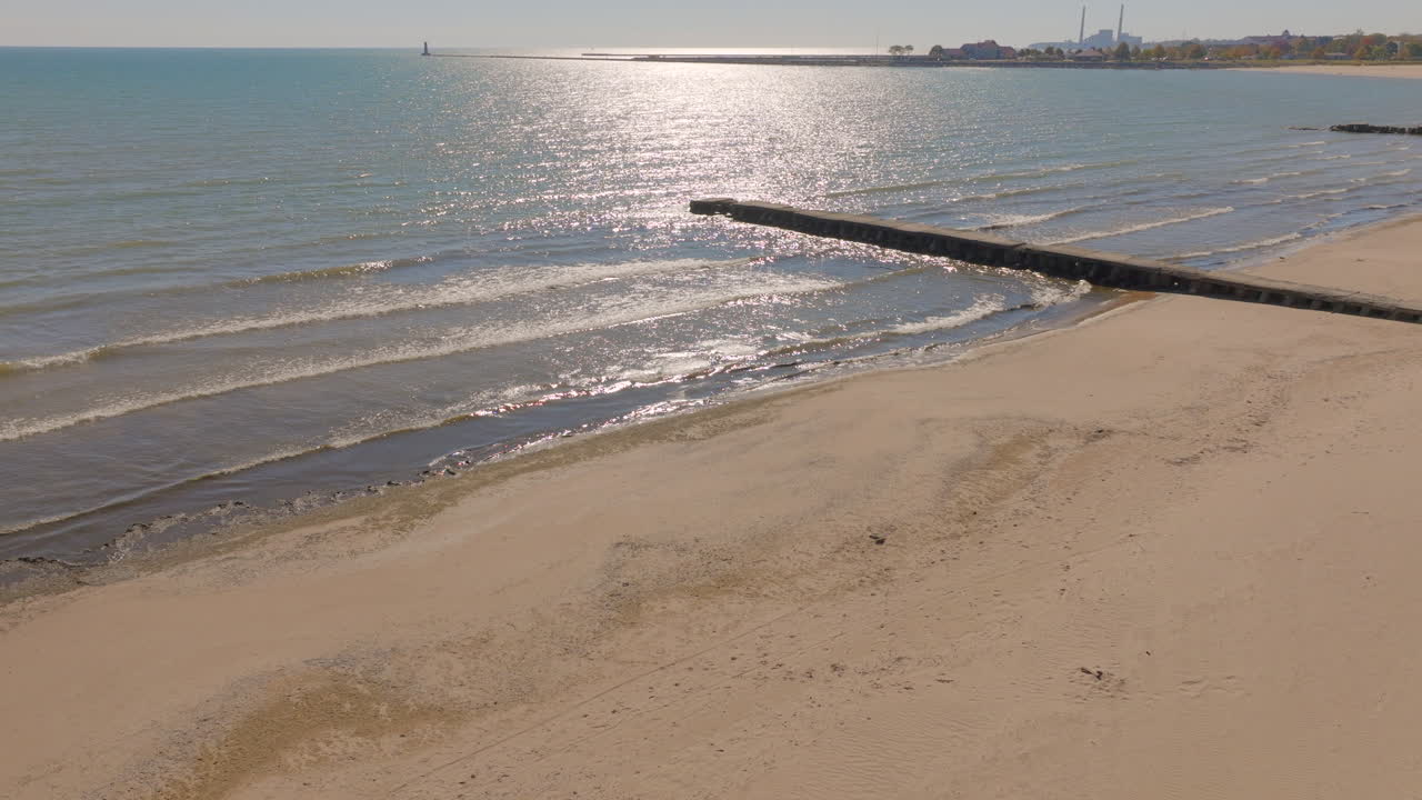 Beautiful Lake Michigan beach scene in Sheboygan, Wisconsin with gentle waves, concrete pier, and sunlight reflecting on the water during a gorgeous clear autumn day