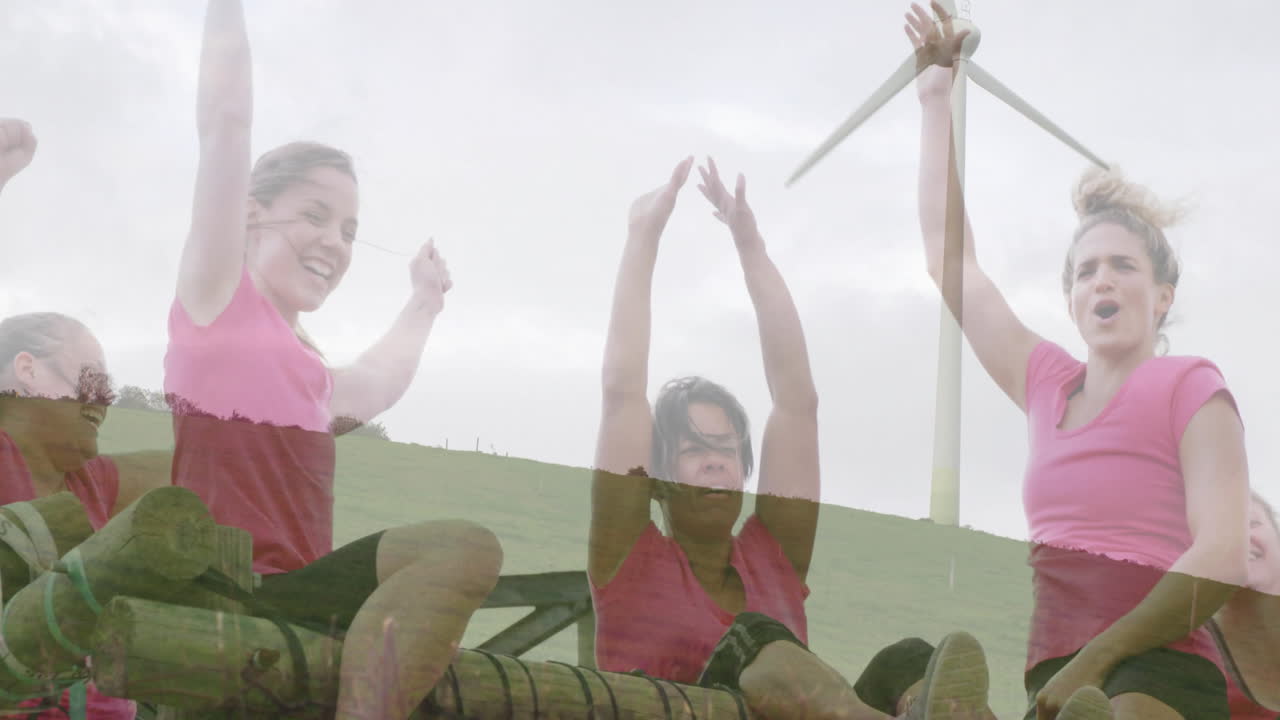 Cheering on obstacle course, women in pink shirts with wind turbine behind