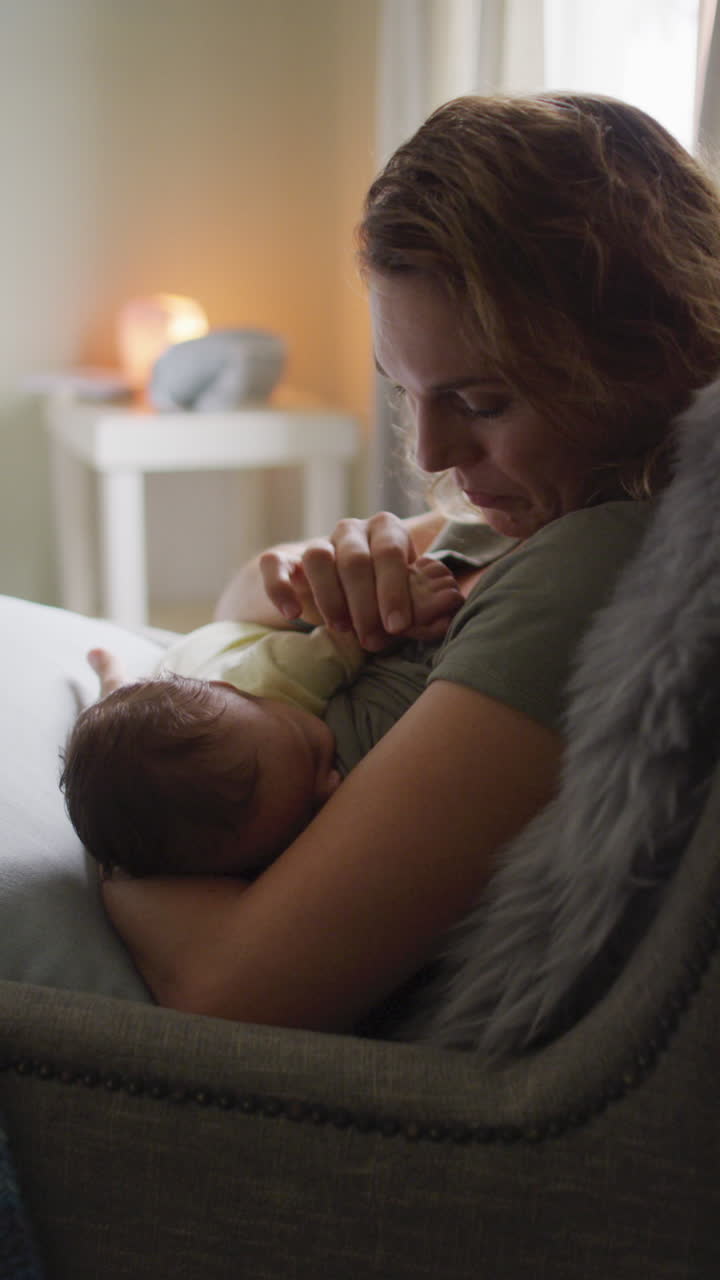 video vertical de una madre caucásica feliz amamantando a un recién nacido en un sillón