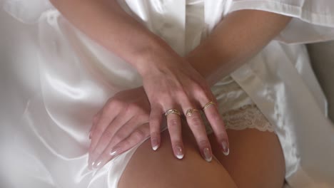 close up of a bride's hands resting gracefully on her lap, adorned with elegant rings, delicate lace, and a silky white robe