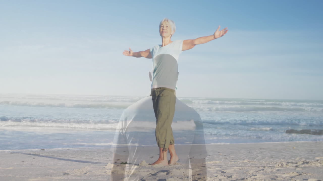 Stretching arms joyfully, elderly woman on beach with ocean waves in background