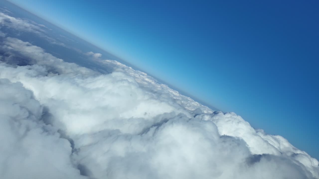 An immersive pilot’s view in a 45-degree left turn over an endless sea of white cumulus clouds, under a blue sky, with a view of the silhouette of the plane inside a raibow on the clouds