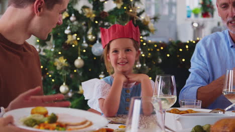 Portrait-Of-Multi-Generation-Family-Celebrating-Christmas-At-Home-Wearing-Paper-Hats-Eating-Meal