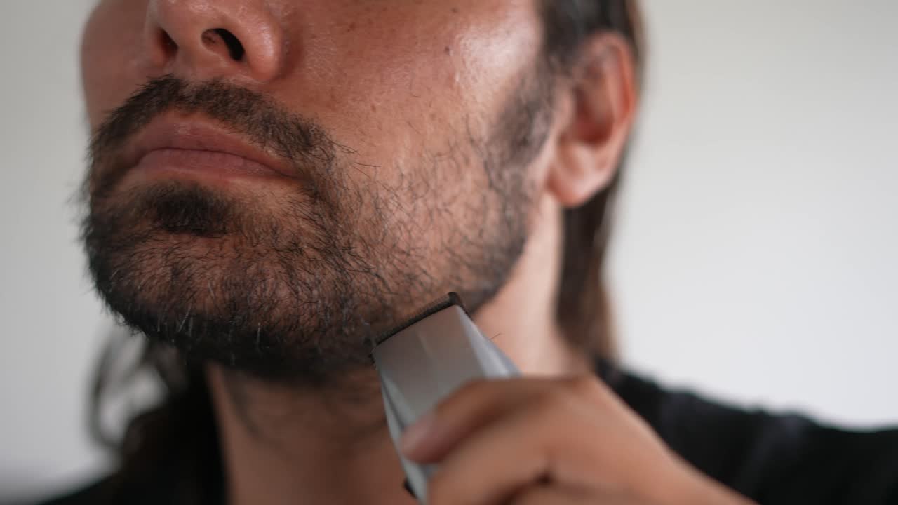 Uomo latino che si taglia barba e baffi con un rasoio elettrico, olio da barba