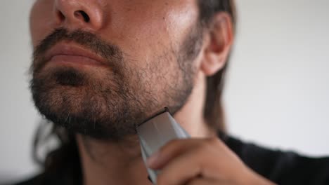 hombre latino recortando barba y bigote con afeitadora eléctrica, aceite de barba