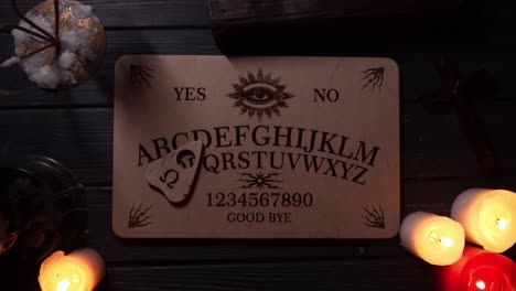 close up video of a wooden ouija board on a table surrounded by candles and a cross in a muffed close up video of a wooden ouija board on a table wax candles and a cross around the planchette is slowly moving across the board spelling out words and numbers creative mystical content