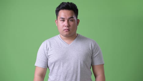 young handsome overweight asian man against green background