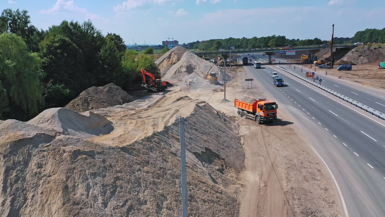 Pile of rubbles near the road. Truck full of stones moving out into the highway. Many cars driving on the road. Aerial view.