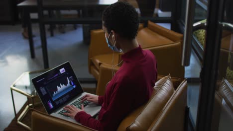 Mujer-Caucásica-Con-Mascarilla-Y-Auriculares-Usando-Una-Computadora-Portátil-En-Una-Oficina-Moderna