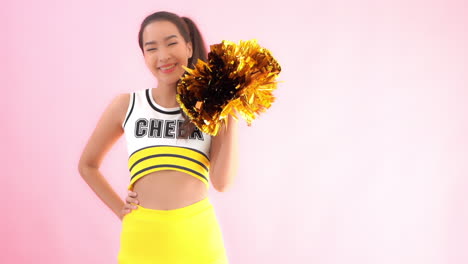 a female cheerleader raises and shakes a single gold and brown pom-pom