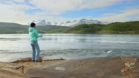 una mujer atrapó un pez grande con una caña de pescar y no puede sacarlo del agua. pescar con una caña de pescar girando en noruega. pescar en noruega es una manera de abrazar el estilo de vida local.