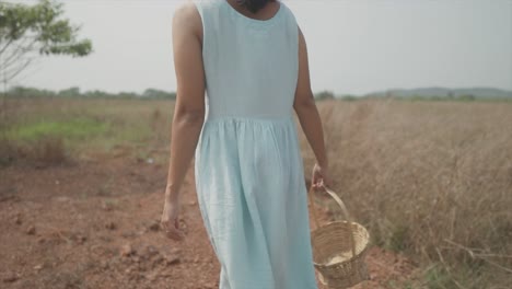 close-up shot of a woman in a blue dress walking in a field with a basket in her hand