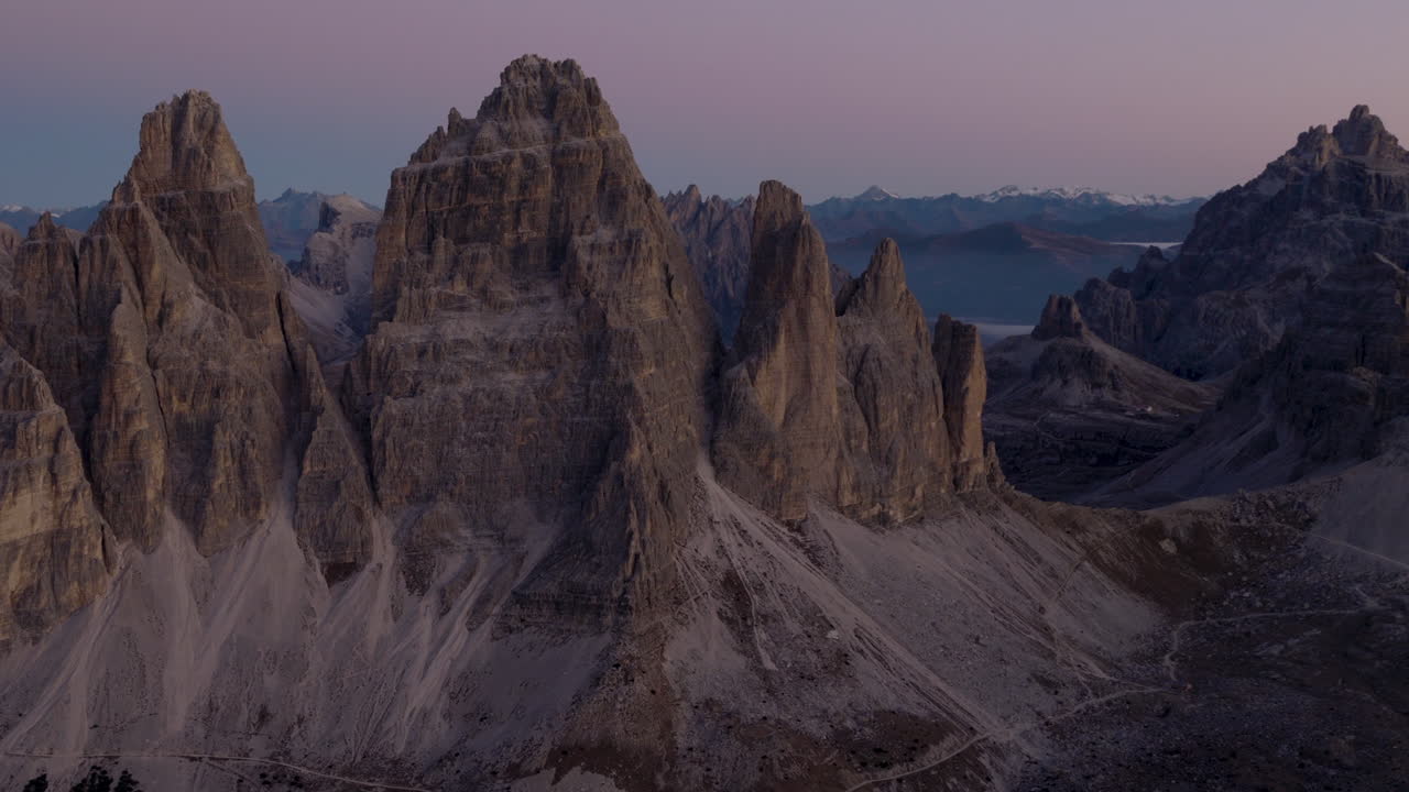 Vista aerea cinematografica delle Dolomiti in Italia, cime alpine frastagliate che si illuminano all'alba, pareti a strapiombo mozzafiato e profonde valli in ombra che creano un'atmosfera serena ad alta quota