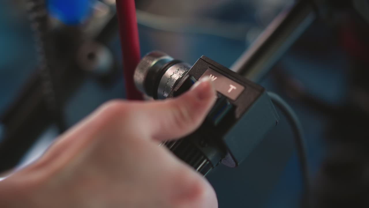 Close-up of hand adjusting camera focus zoom control on professional camera rig in broadcast studio. Button labeled W and T, highlighting operator's precise control over filming process