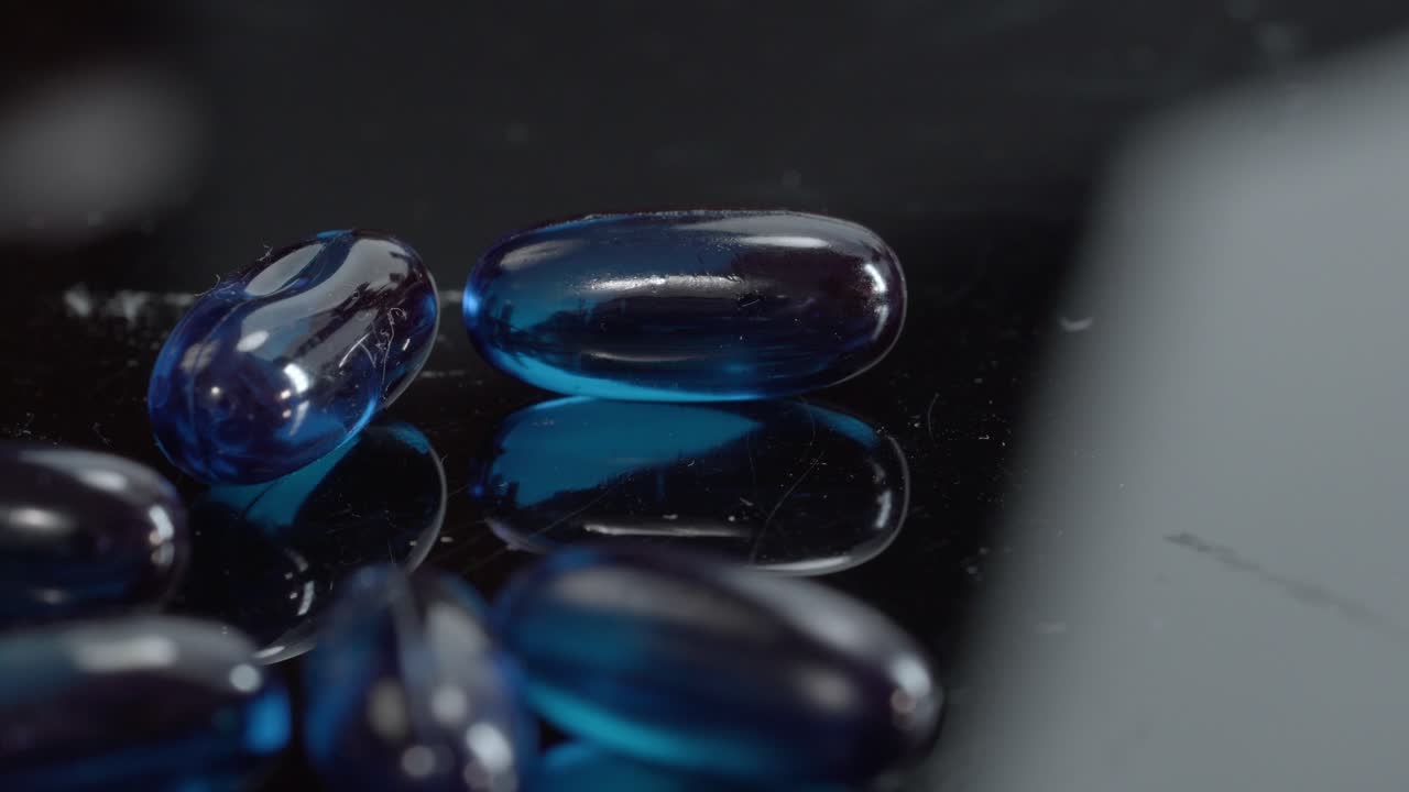 Close up of blue gel medicine capsules placed on reflective black surface, studio lighting