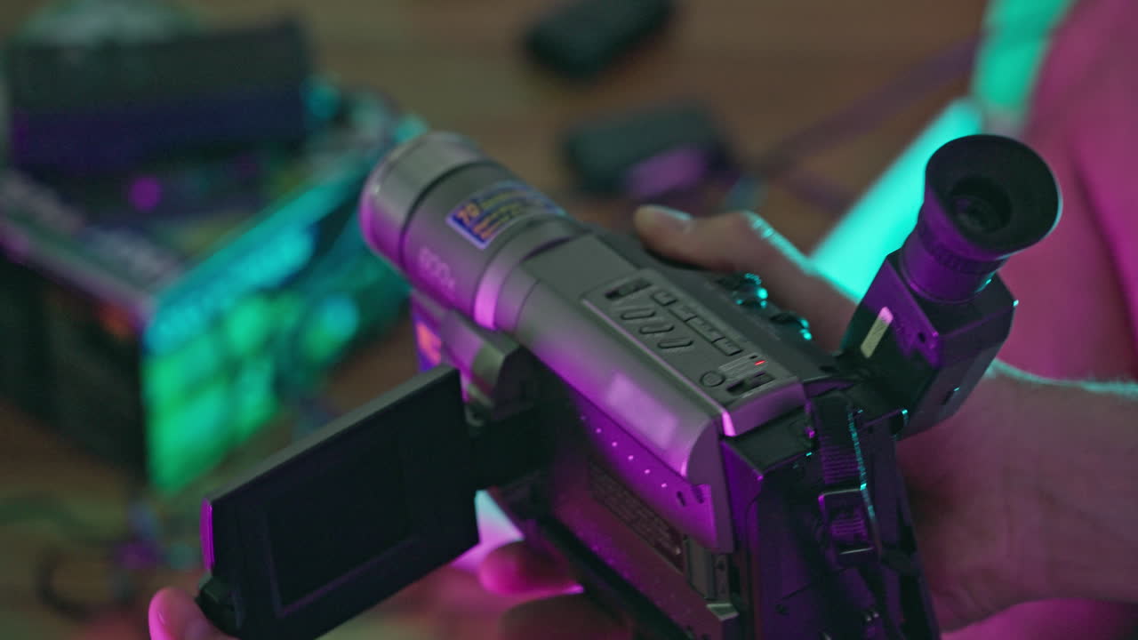 Person's Hands Operating a Vintage Camcorder Under Neon Lights
