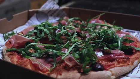 close-up of a delicious pizza in box, while the chef adds arugula, also known as rocket, as a topping