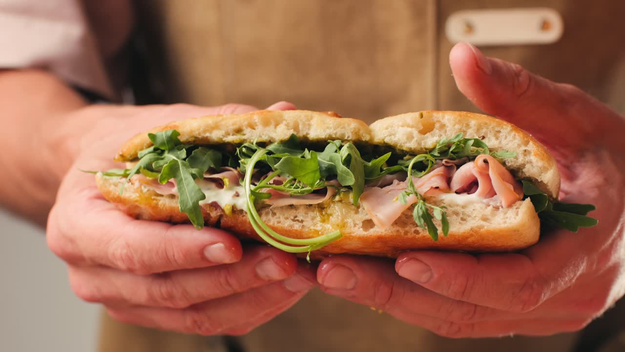 Mortadella ham sandwich, Traditional italian focaccia filled with thin pesto slices of mortadella, served by chef man in cafe restaurant. Macro of traditional italian spanish tapas antipasti.