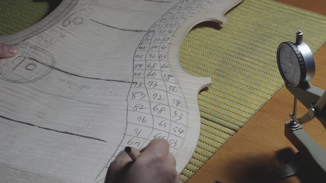 fabricante de instrumentos de cuerda maestro luthier proceder con el trabajo de graduación en la placa trasera del violonchelo, usar calibre medidor de grosor, medir niveles, usar lápiz escribir valores en madera, taller de cremona, italia