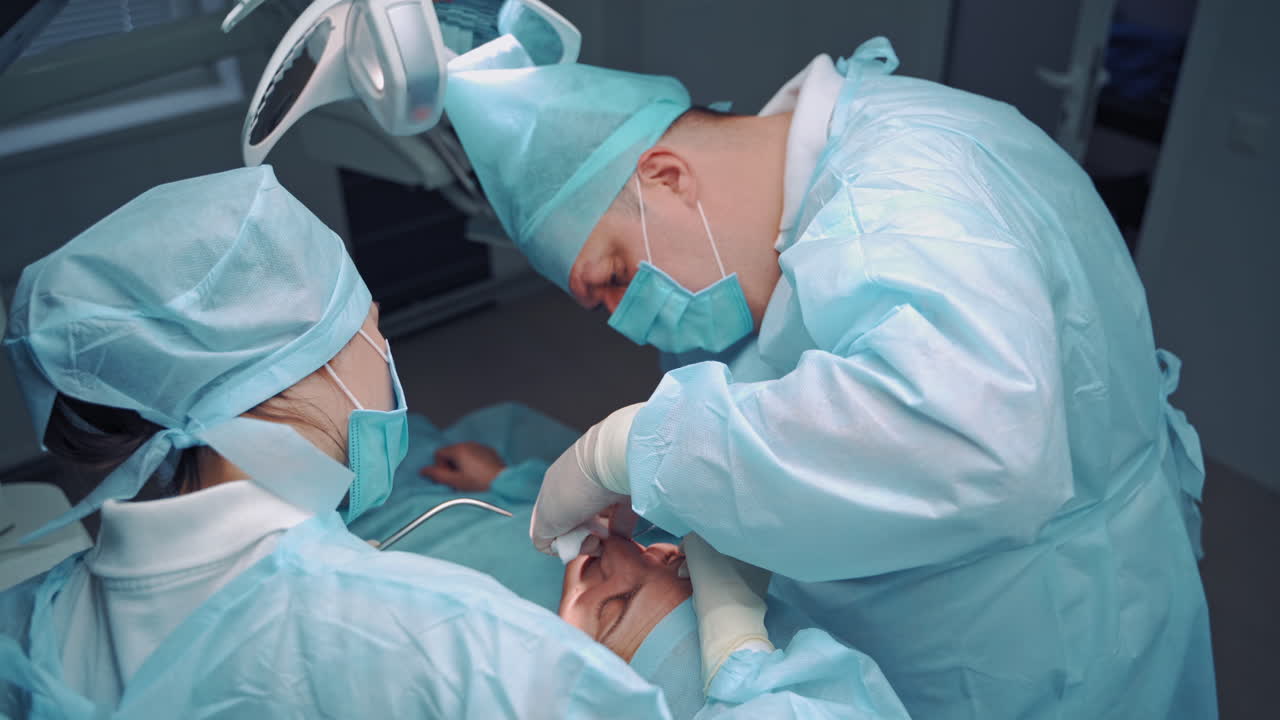 Dental specialist and assistant in medical uniform work in stomatology center. Doctor and female nurse making medical treatment on teeth for patient. Oral surgary.
