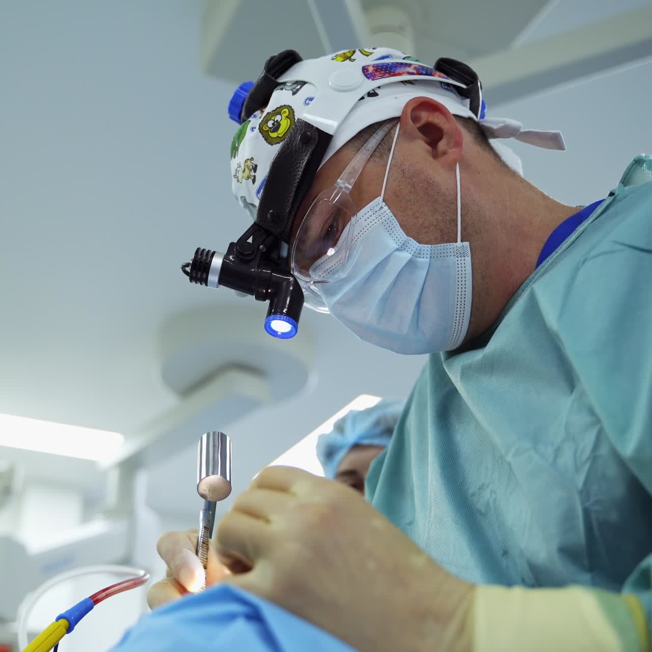 Experienced doctor in device glasses holding metal tool. Nurse hits the instrument in doctor's hands with little metal hammer. Low angle view