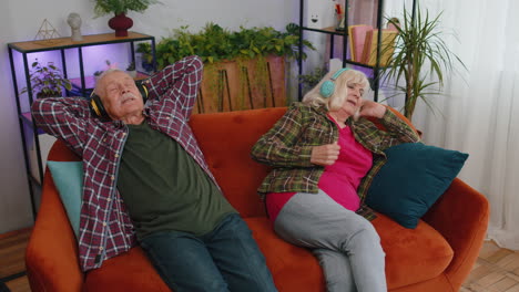 happy senior family grandparents man woman in headphones listening music relaxing on couch at home