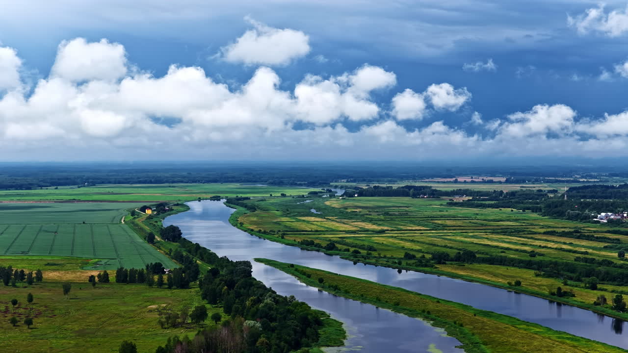 Pan drone shot of beautiful landscape of rivers winding through vast agricultural fields with cumulus clouds in sky