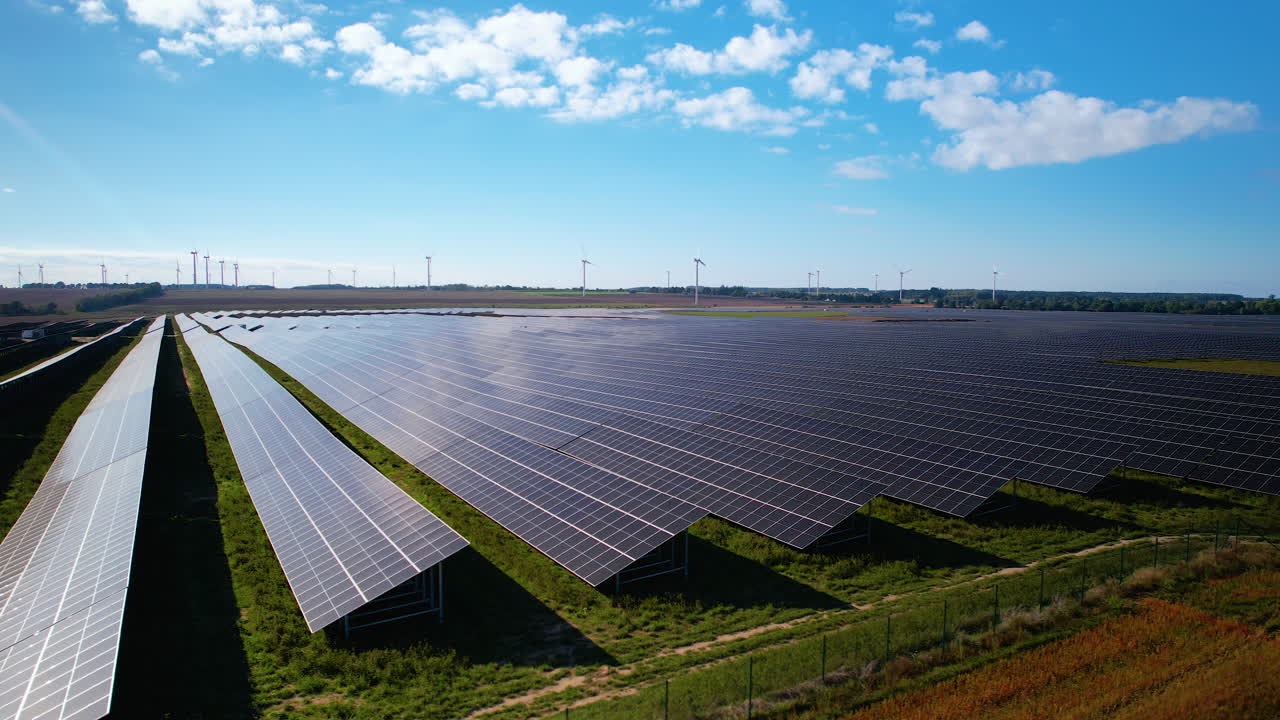 Flyvende optagelse af moderne solcellepark på landlig mark og vindmøllepark i baggrunden om sommeren