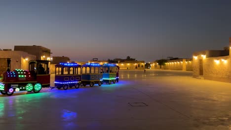 A-surreal-scene-landscape-a-kid-train-normally-in-amusement-park-but-in-Qatar-Doha-Wakrah-Waqif-old-city-at-night-carry-carriage-wagon-in-the-street-neon-light-old-houses-warm-yellow-color-traditional