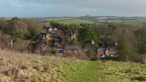 a hiker hikes on hilltop with view of a beautiful village nestled in rolling hills, forests and national park in background