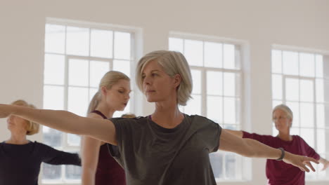 yoga class of healthy mature women practicing warrior pose enjoying physical fitness workout instructor teaching group in exercise studio